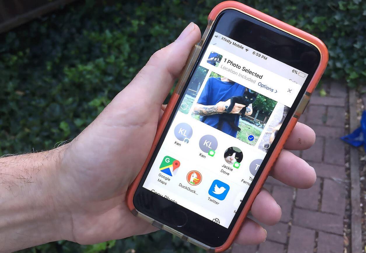 Как удалять геолокационные метки с фото и видео в iOS 13? iPhone В руке с запущенным приложением Фото. Фото.