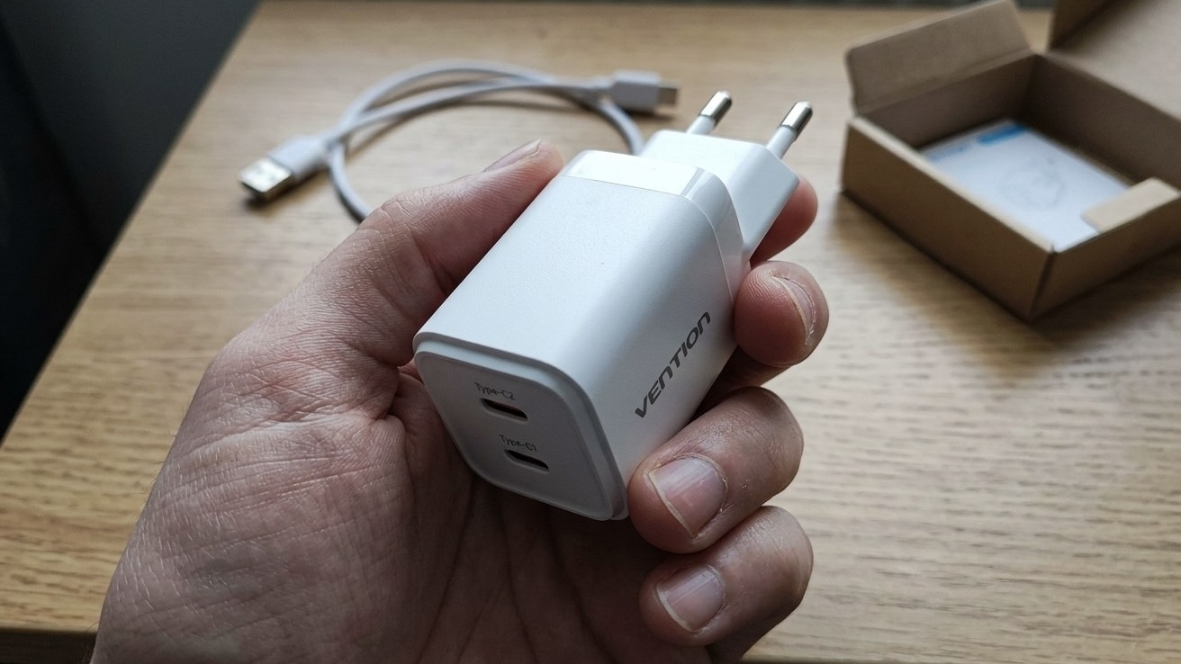 Белая зарядка Vention с двумя портами USB-C в руке, рядом кабель и коробка