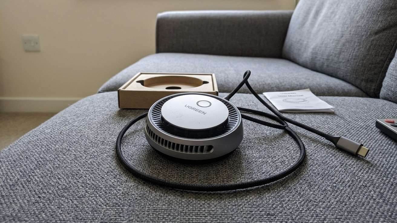 Магнитная зарядка UGREEN MagFlow Pro с вентиляционной решеткой по кругу лежит на сером диване рядом с коробкой и кабелем USB-C