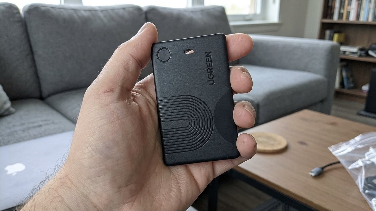 Черная метка UGREEN Finder Slim 2 размером с банковскую карту в руке на фоне дивана