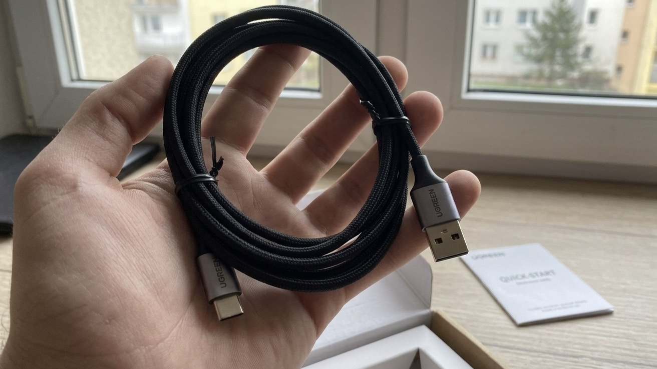 Свернутый кабель UGREEN USB-A — USB-C в черной оплетке лежит на ладони у окна