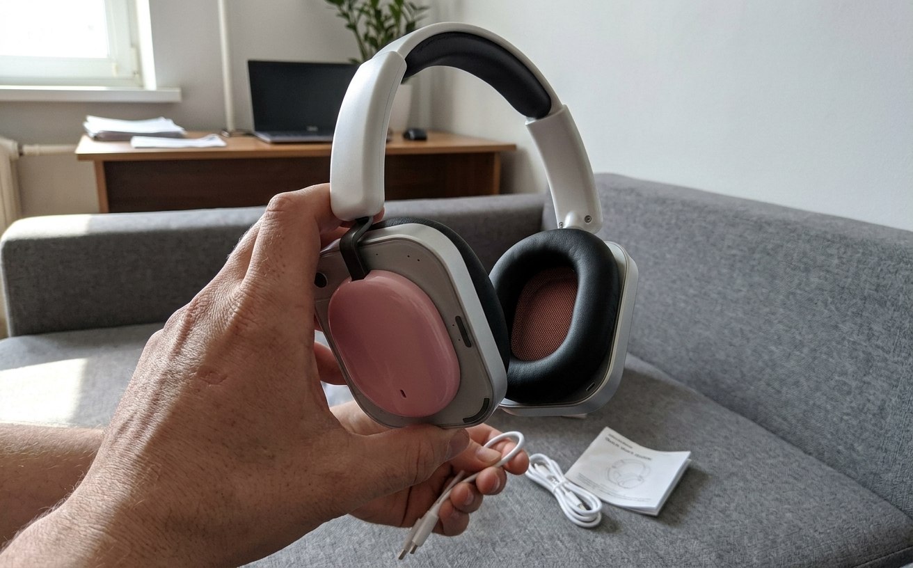 Человек держит белые наушники Nothing Headphone (a) с розовыми чашками, на диване лежат кабель и инструкция