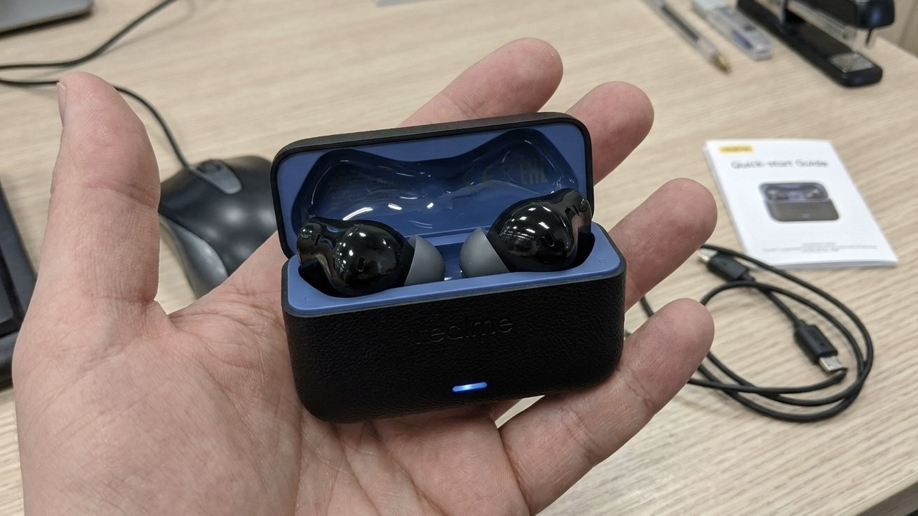 Наушники realme в черном кейсе с синей внутренней частью на ладони, рядом кабель и инструкция