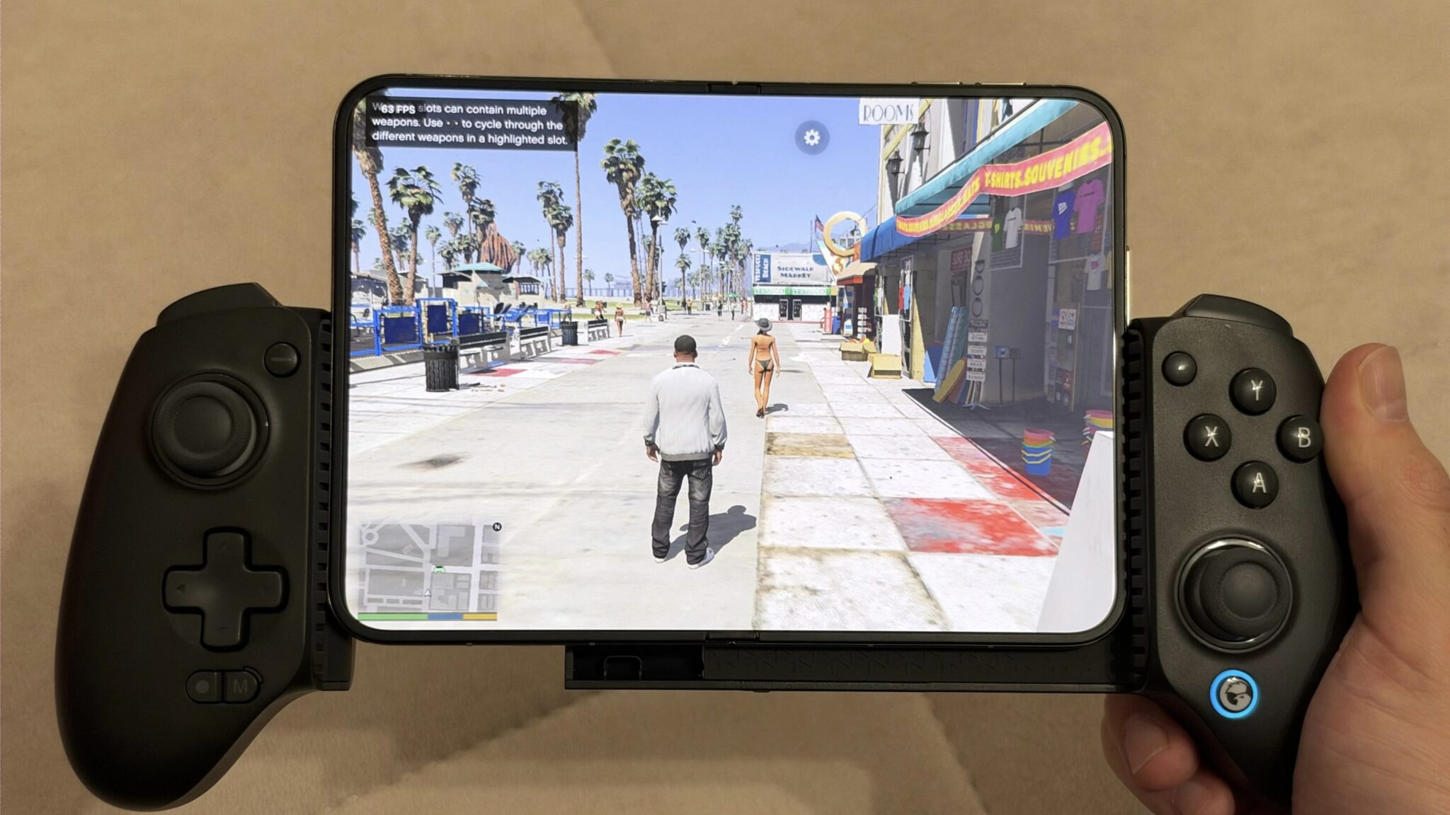 Складной смартфон с GTA V вставлен в геймпад-держатель, персонаж идет по набережной Веспуччи. Изображение: BenGeskin