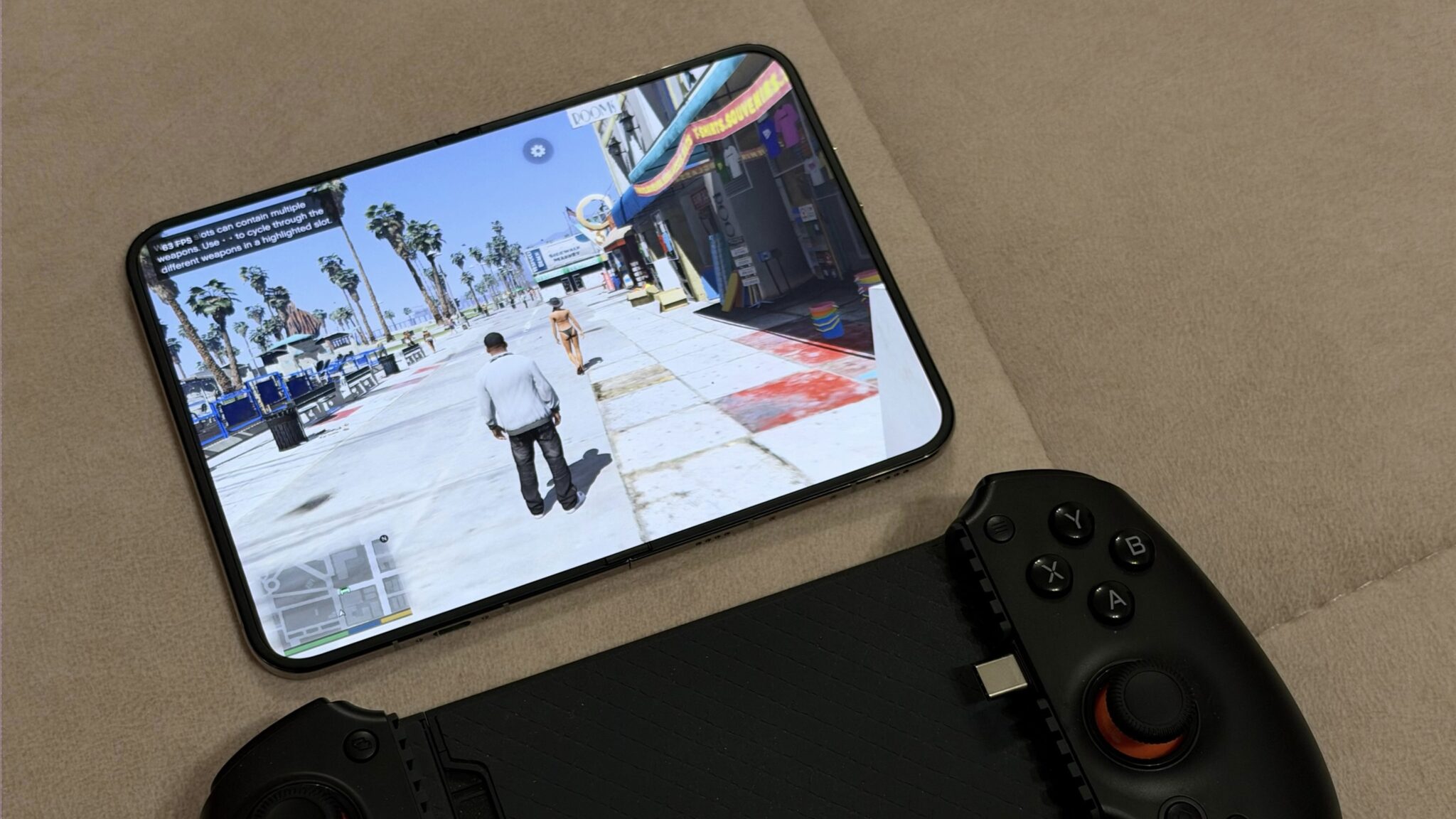 Смартфон с запущенной GTA V лежит на диване рядом с геймпадом. Изображение: BenGeskin