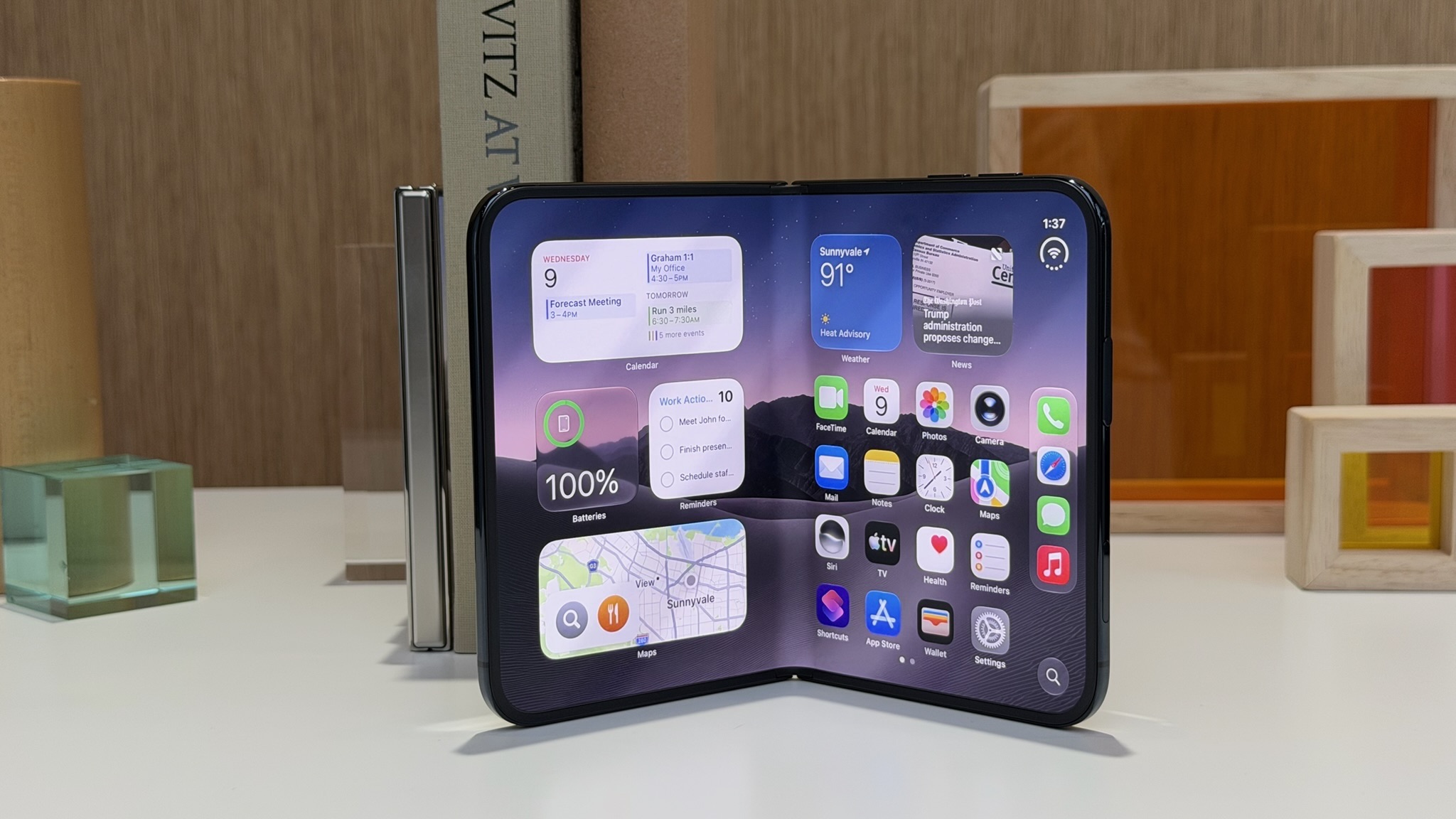 Наполовину сложенный iPhone Duo стоит на столе, экран согнут по линии шарнира