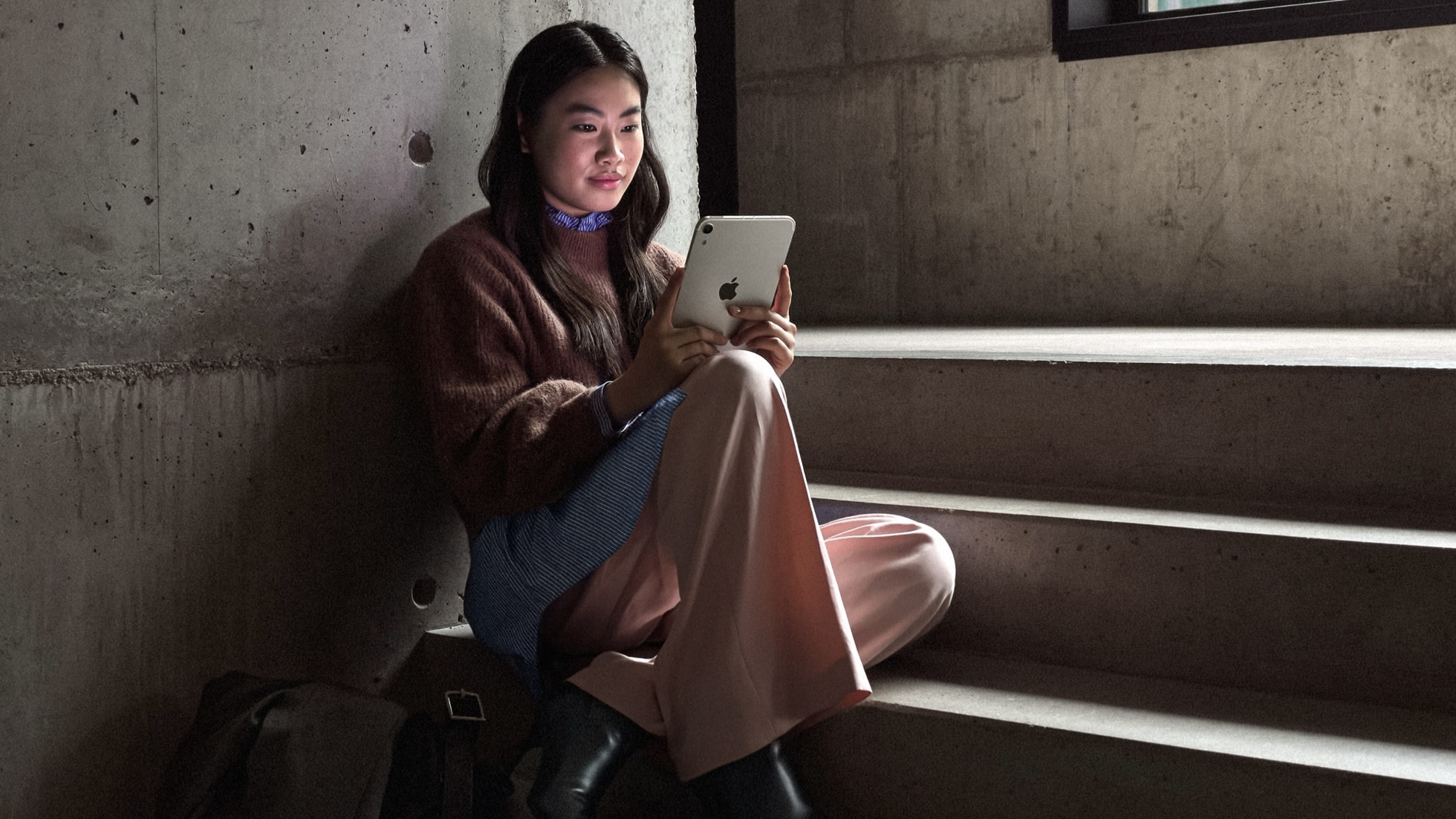 Девушка сидит на бетонной лестнице в полутемном помещении и читает с iPad mini