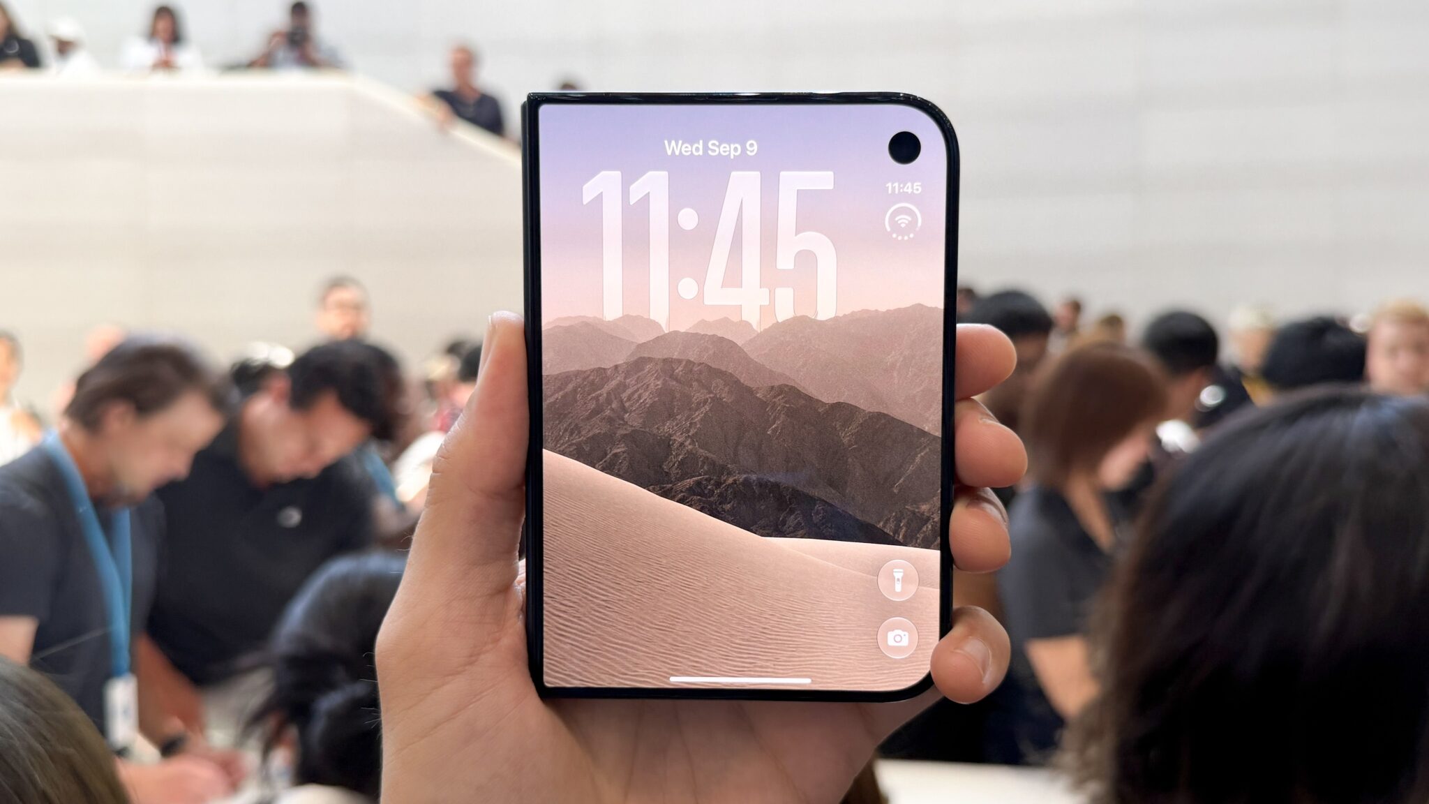 Сложенный iPhone Duo в руке: на внешнем экране часы, в правом верхнем углу вырез фронтальной камеры