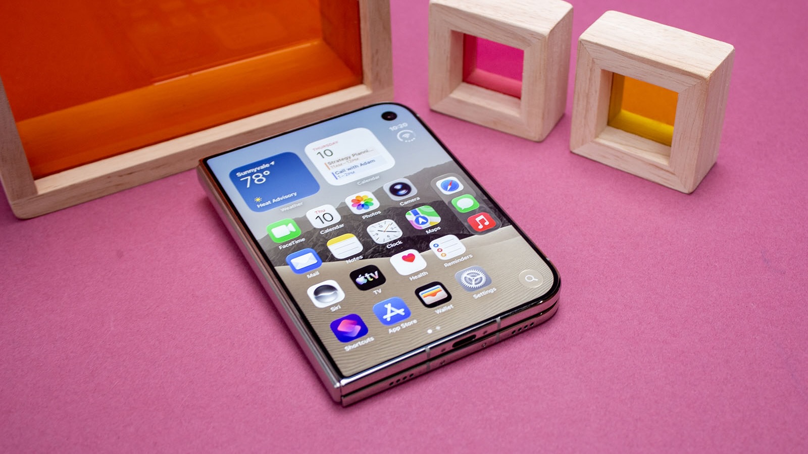 Раскрытый iPhone Duo лежит на розовом столе рядом с деревянными рамками
