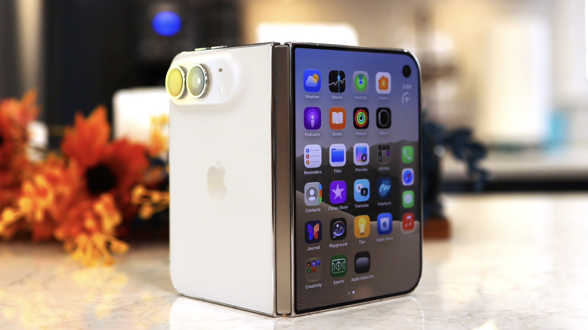 Белый iPhone Duo стоит на столе в раскрытом наполовину виде, за ним букет осенних цветов
