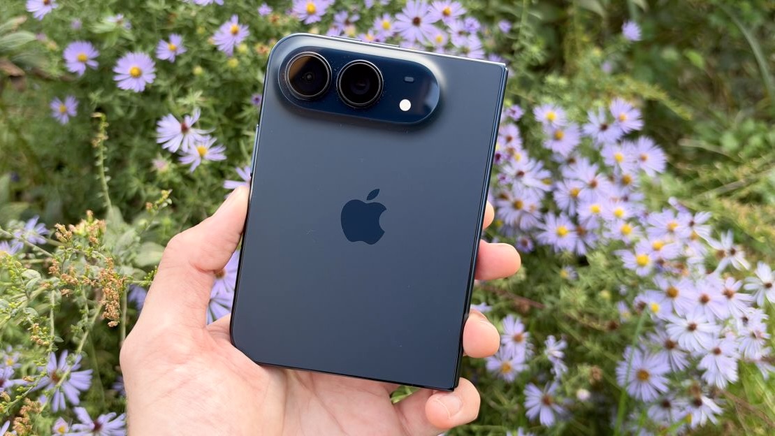 Задняя панель iPhone Duo цвета Night Sky с двумя камерами в руке на фоне цветов