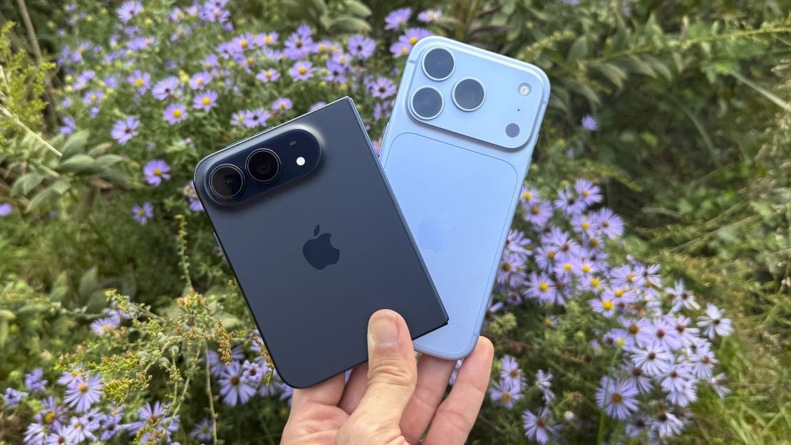 Темно-синий iPhone Duo и голубой iPhone 18 Pro в руке на фоне цветущих астр