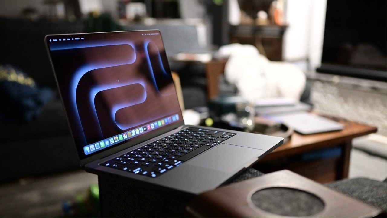 MacBook Pro в цвете «космический черный» стоит на подлокотнике дивана в полутемной комнате