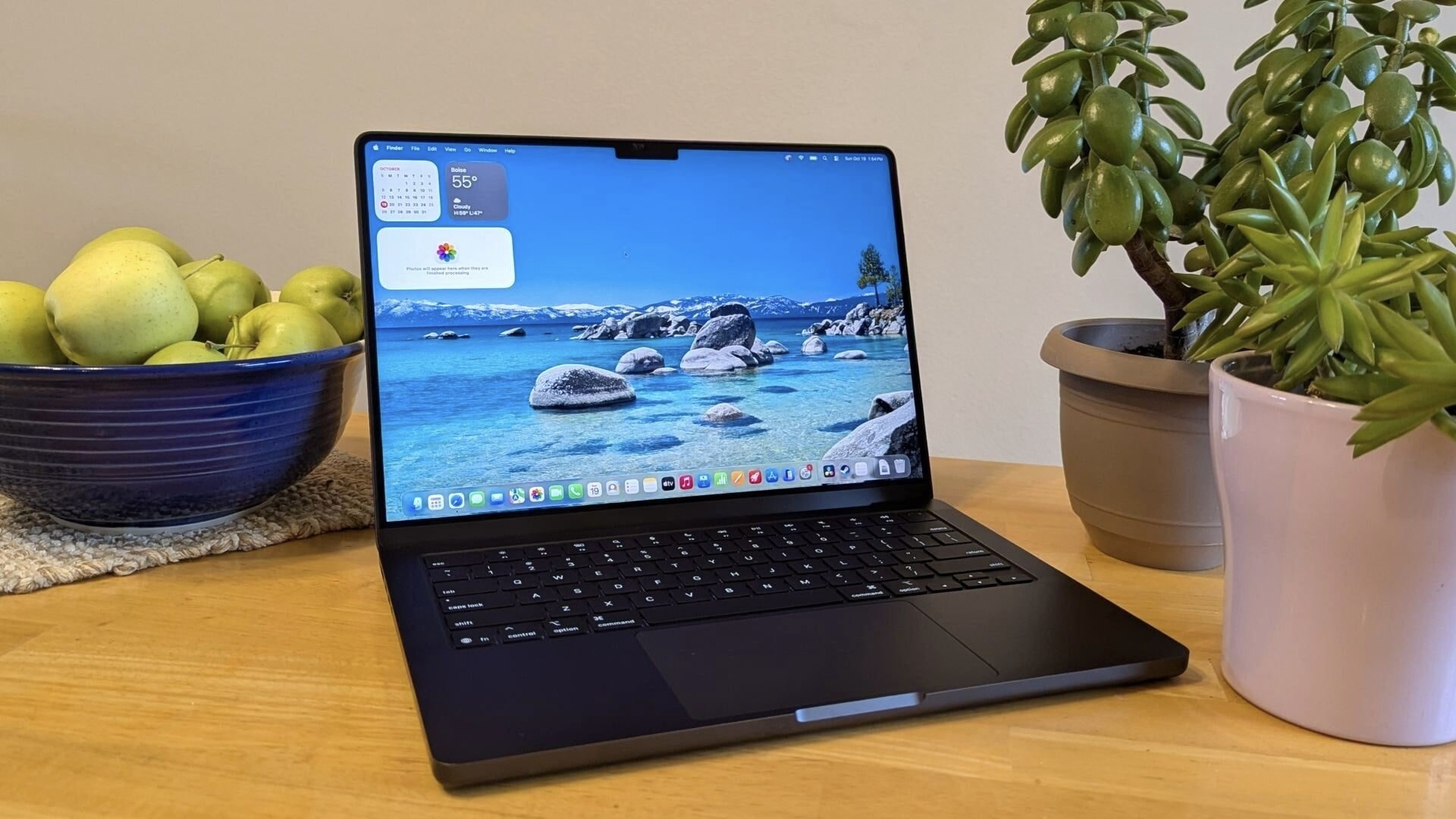 Черный MacBook Pro на деревянном столе между миской с яблоками и комнатными растениями