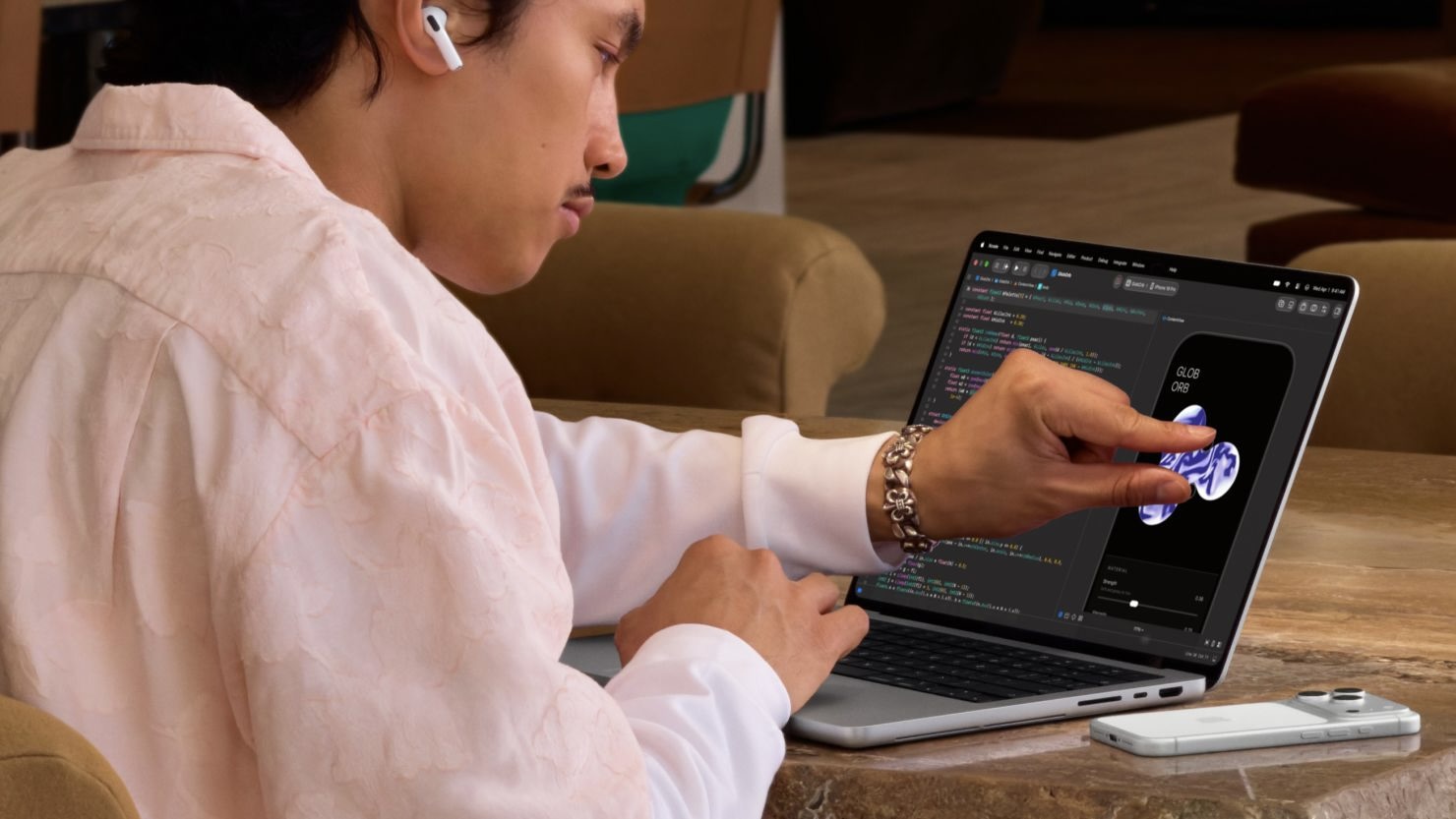 Мужчина одной рукой печатает на клавиатуре MacBook Pro, а другой касается экрана с приложением для iPhone