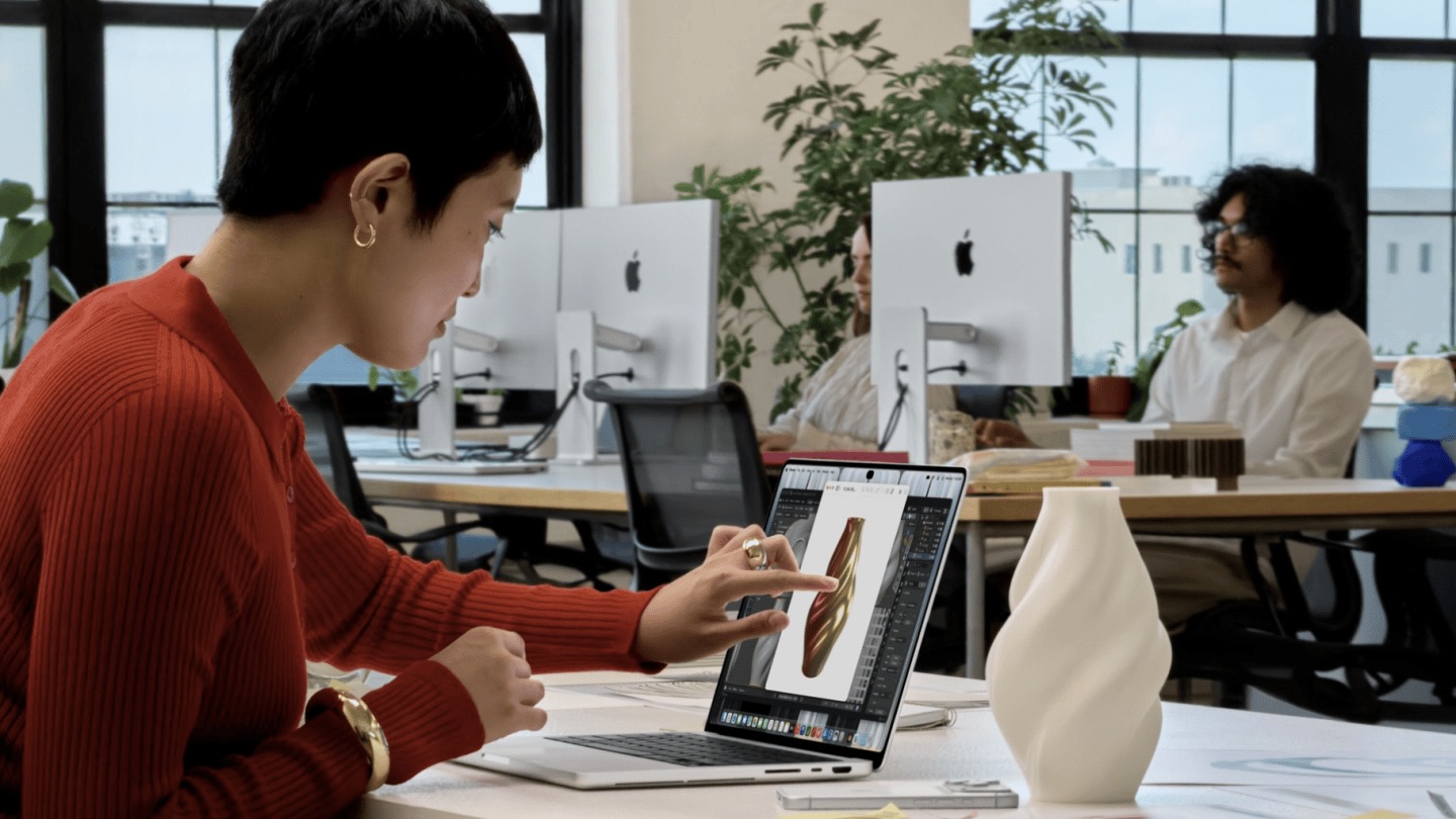 Девушка в офисе вращает пальцем 3D-модель вазы на экране MacBook Pro