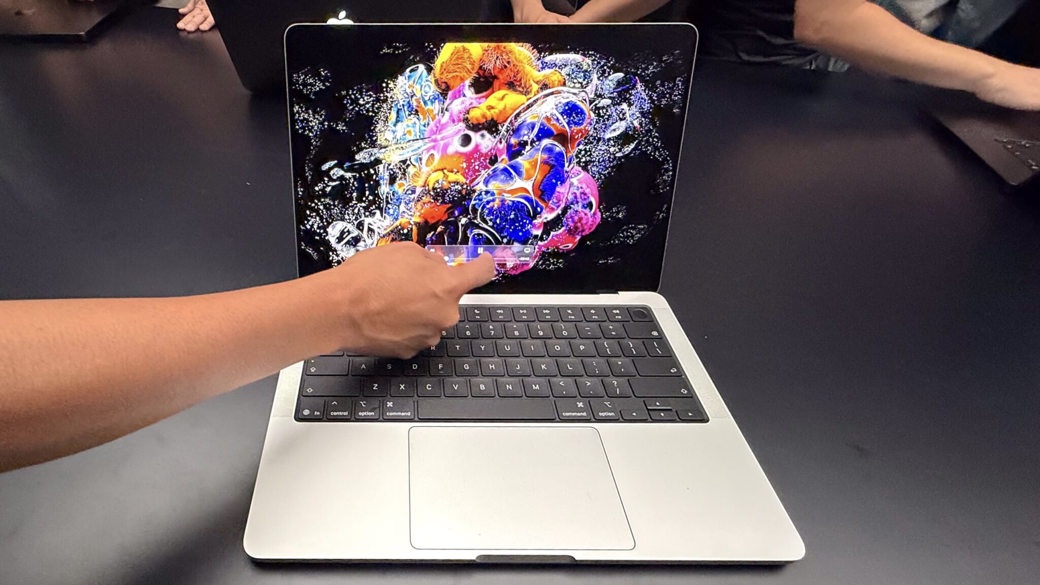 Человек касается пальцем экрана серебристого MacBook Pro с PROLED XDR