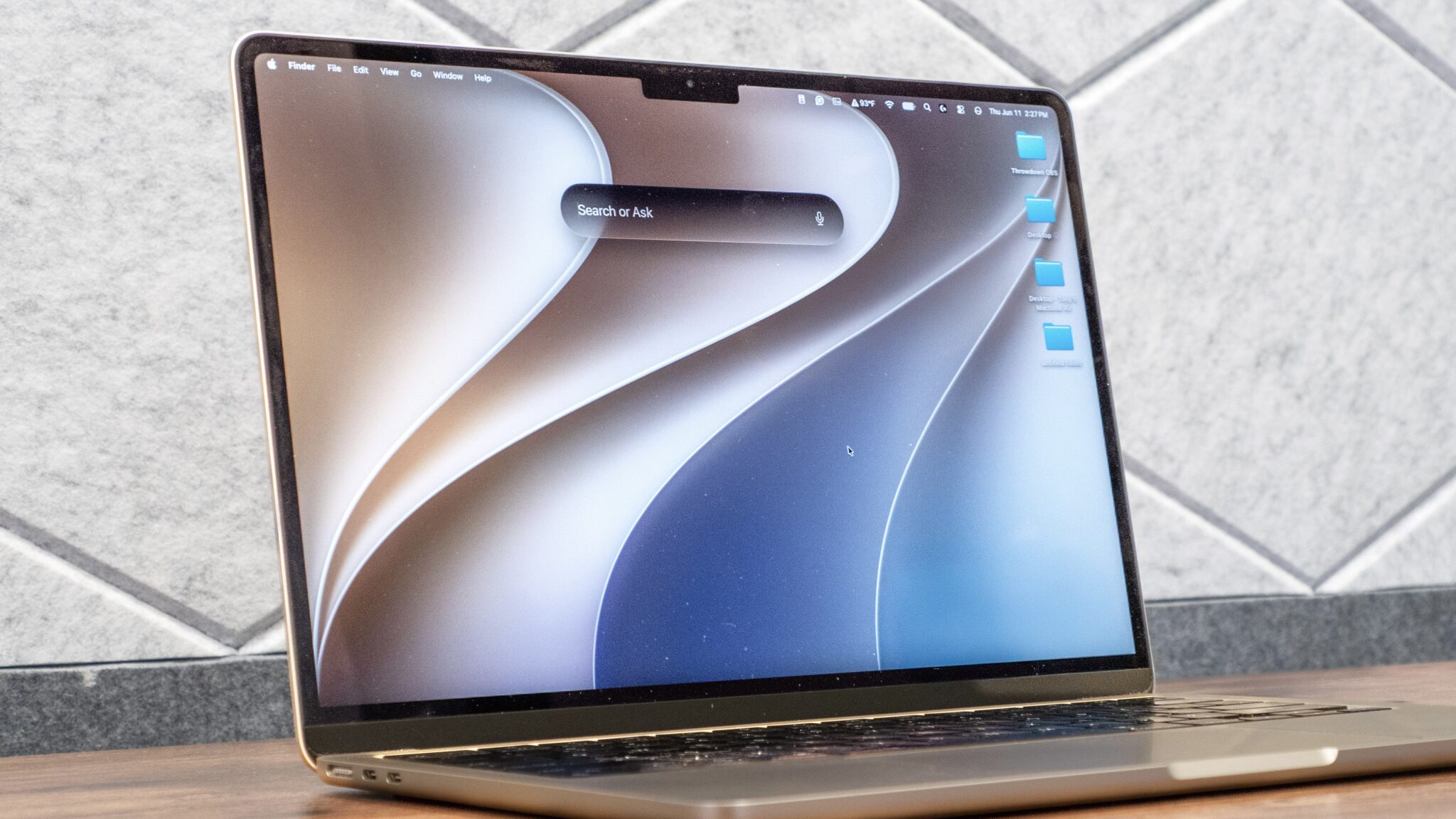 MacBook Air на столе: посреди рабочего стола открыта строка Siri AI с подсказкой Search or Ask
