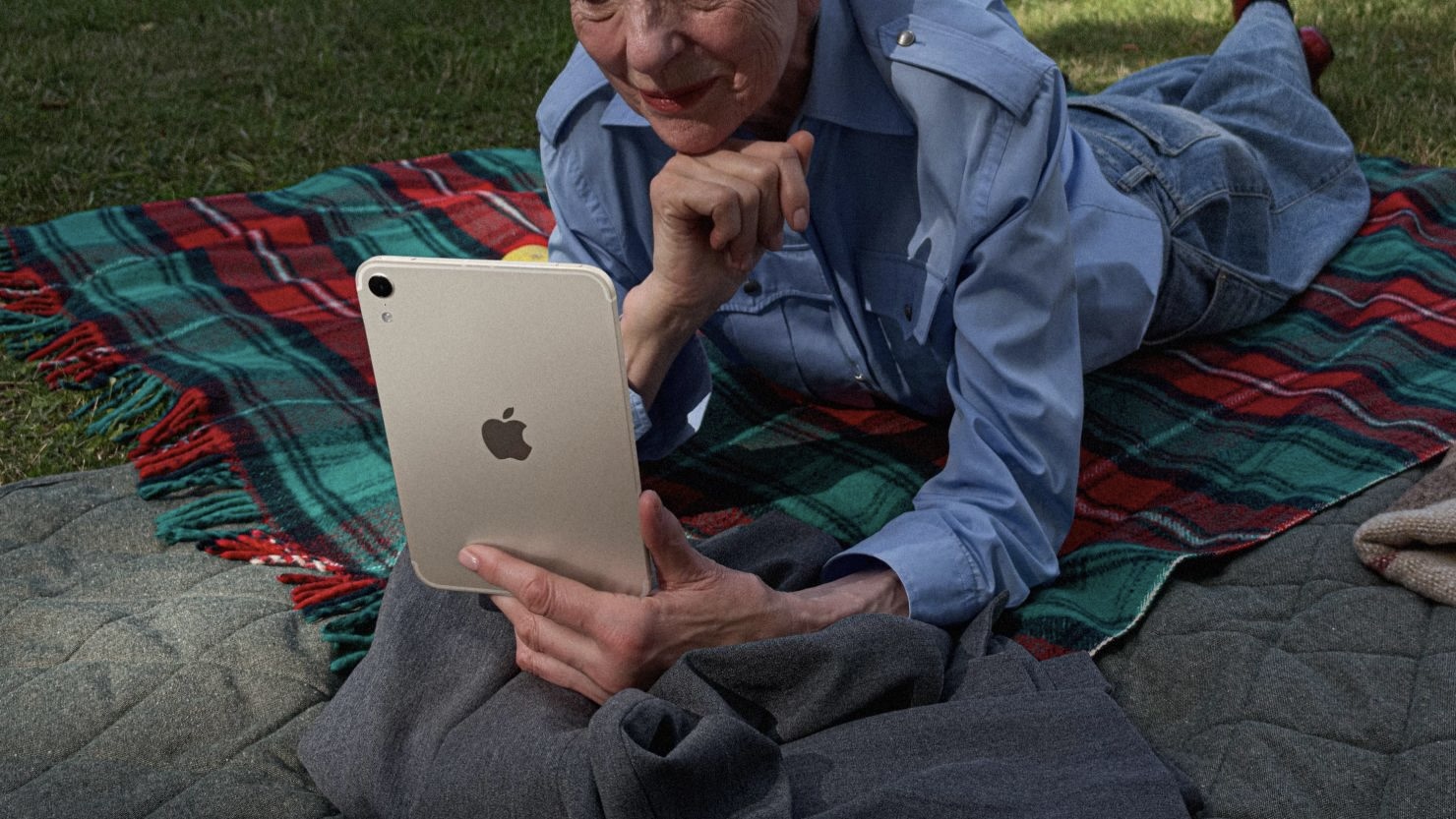 Женщина лежит на пледе в парке и смотрит в iPad mini цвета «сияющая звезда»