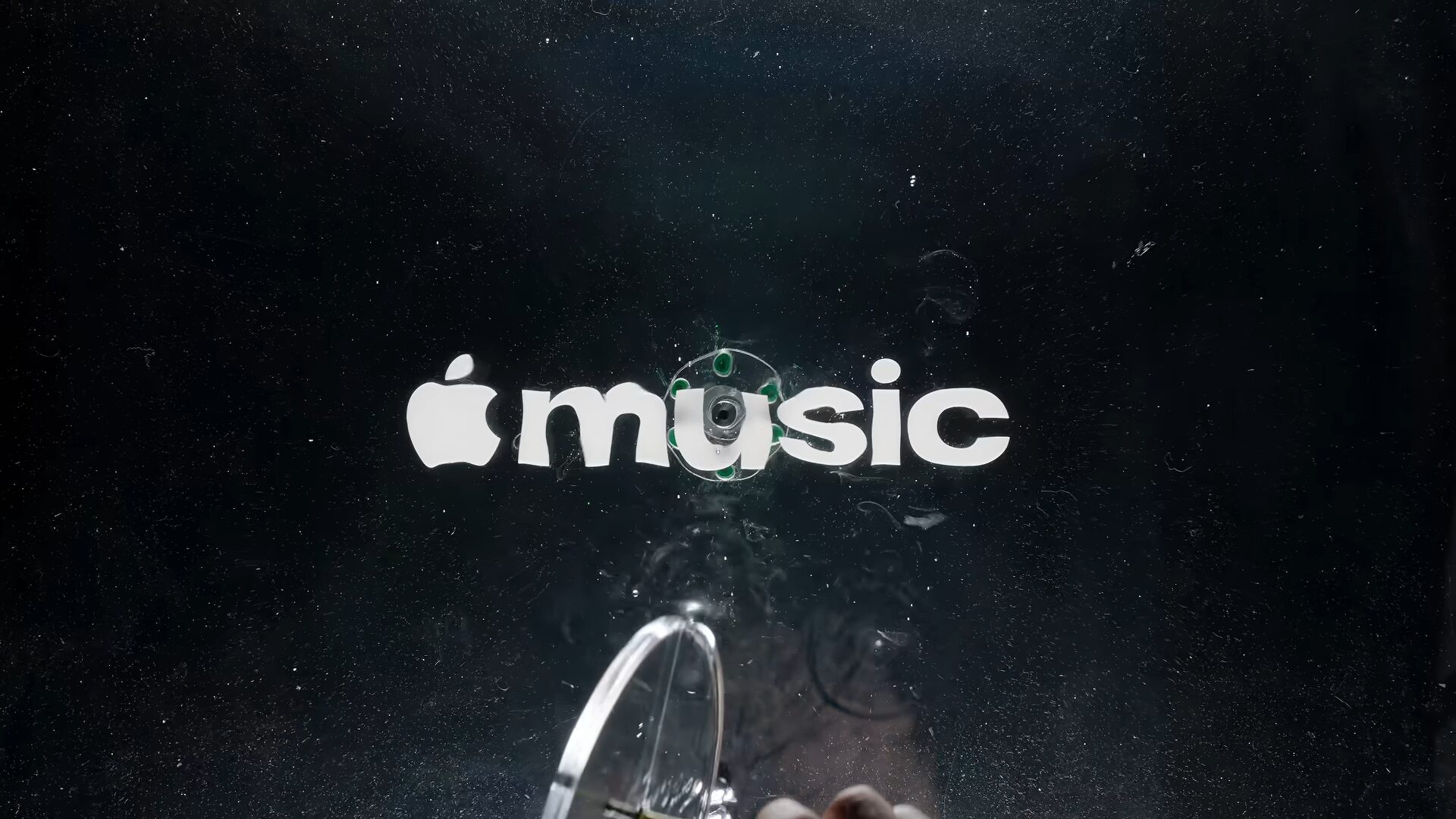 Белый логотип Apple Music под колеблющейся жидкостью, в центре виден преобразователь звука