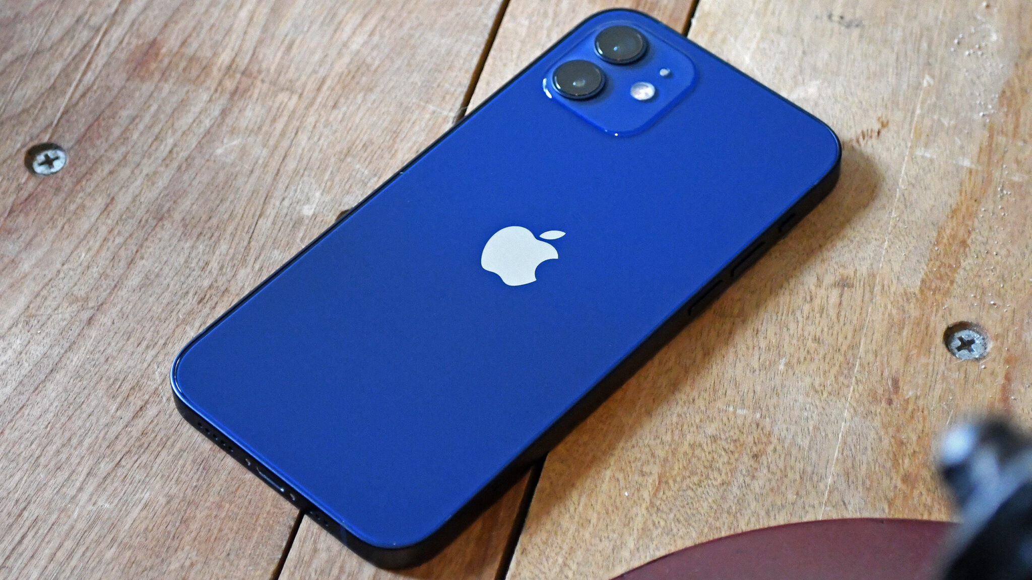 Синий iPhone 12 лежит задней панелью вверх на деревянном столе: с этой модели в айфонах появились магниты MagSafe
