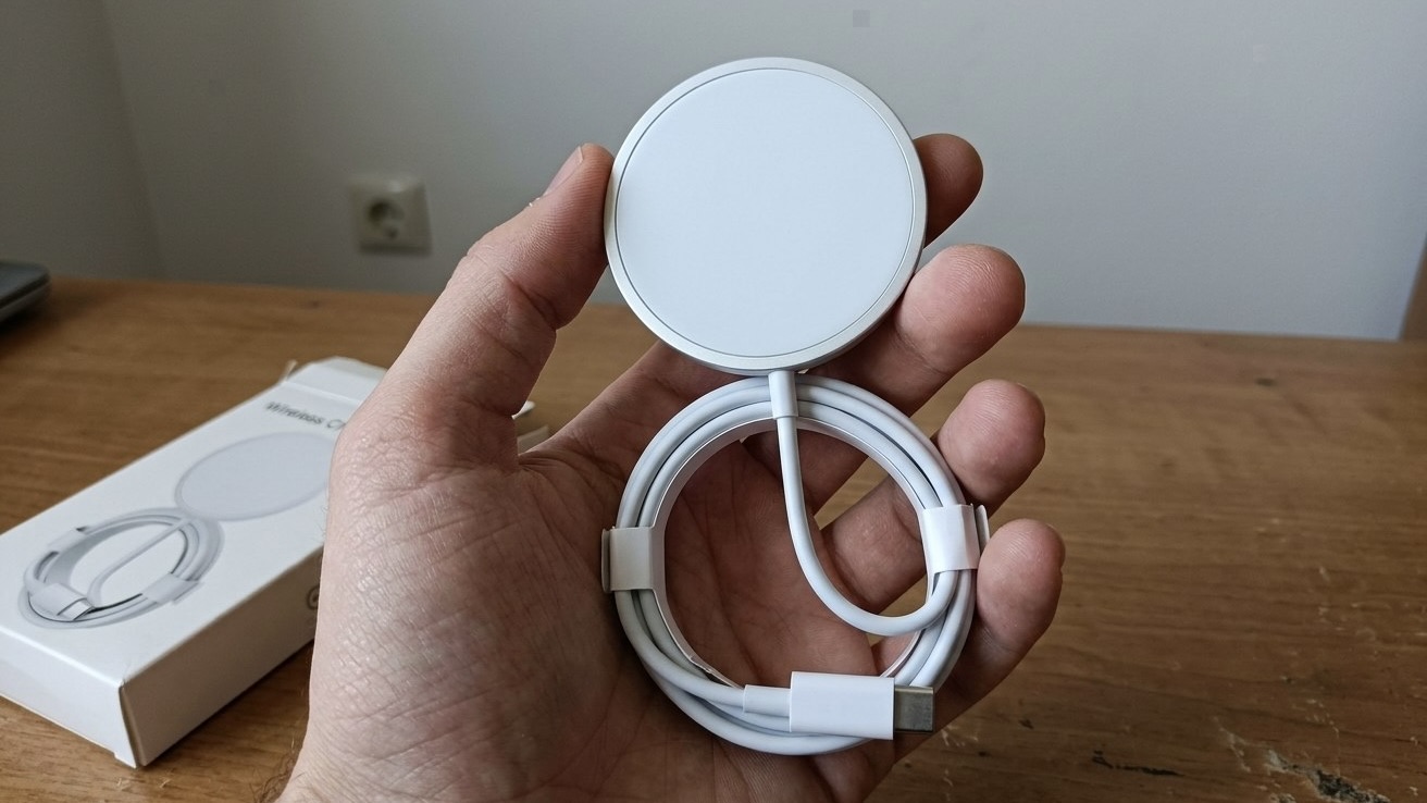 Белая магнитная зарядка на 15 Вт со смотанным кабелем USB-C в руке, на столе рядом лежит ее коробка