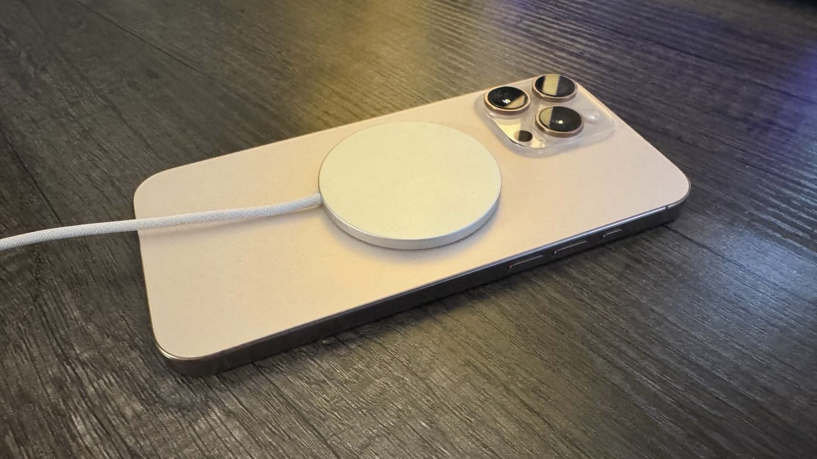 Оригинальная белая зарядка MagSafe с плетеным кабелем примагничена к задней панели iPhone на темном столе