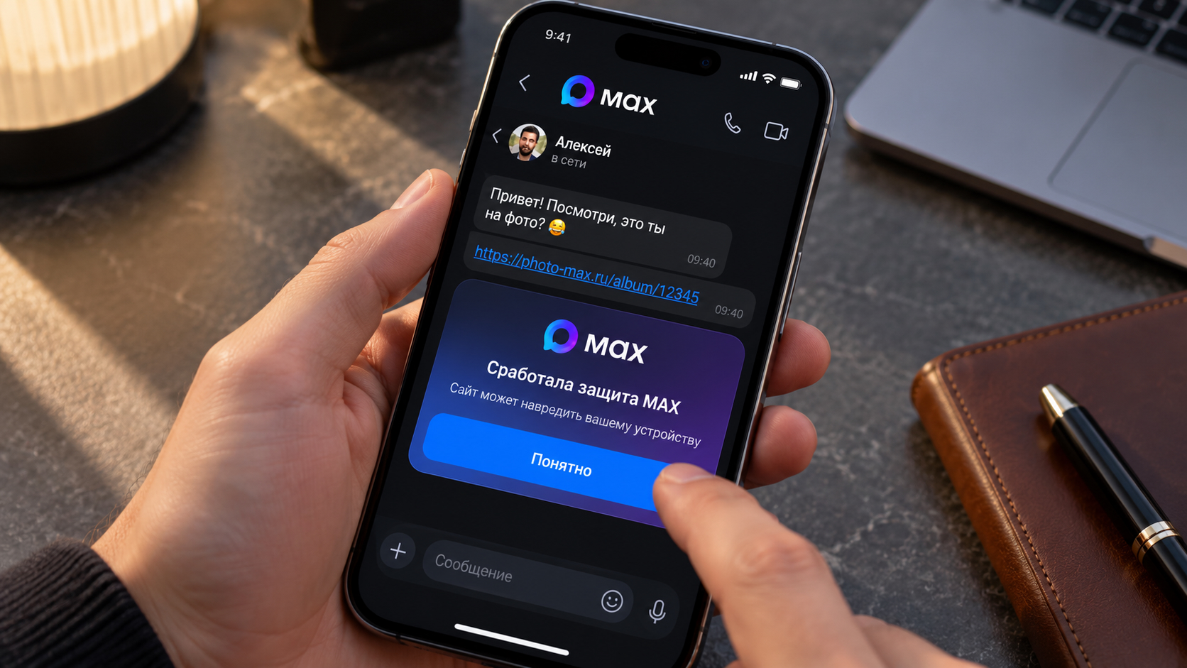 Человек держит iPhone с открытым чатом в МАКС, поверх ссылки всплыло окно «Сработала защита MAX»